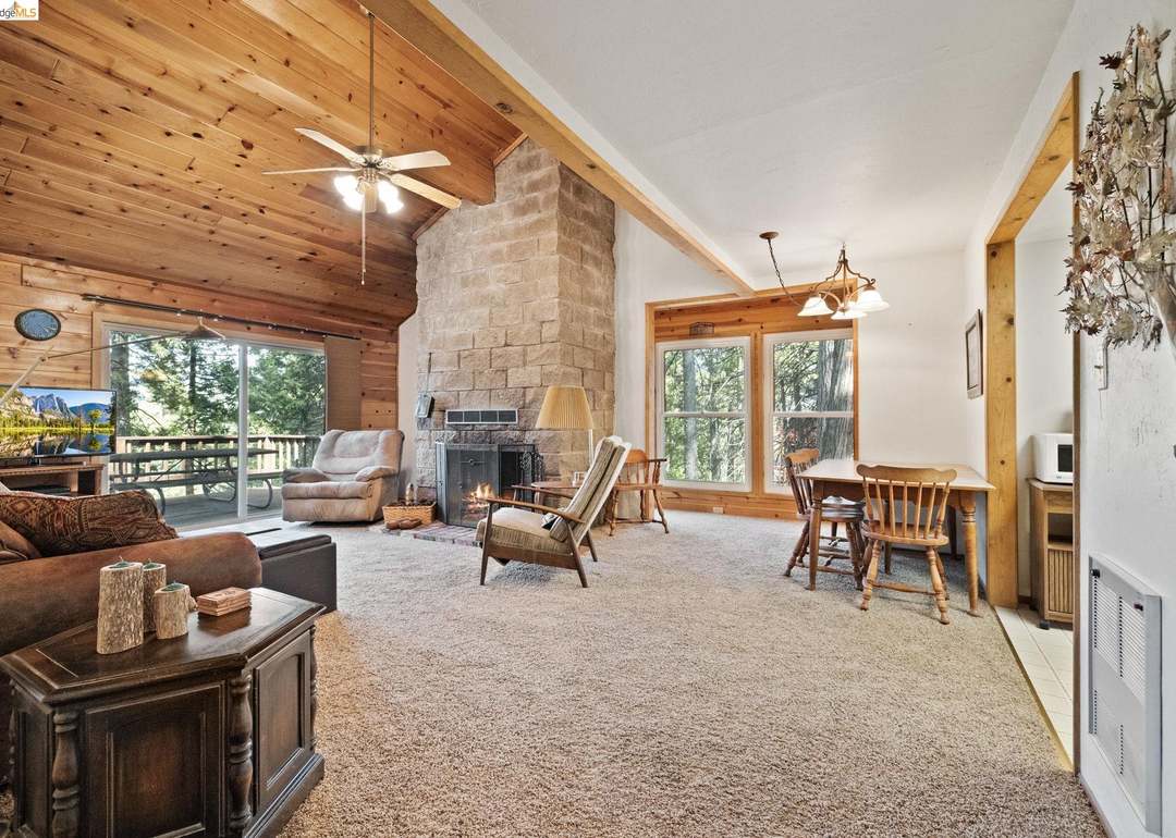 Living room with vaulted wood ceiling, stone fireplace, and sliding doors to the deck